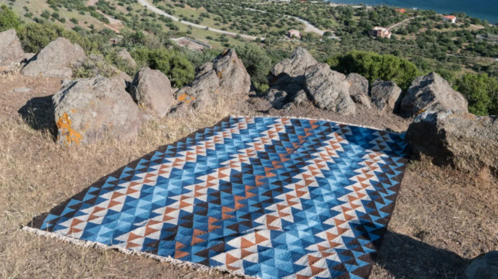 Geometric blue and brown Turkish washable area rug displayed outdoors with coastal view