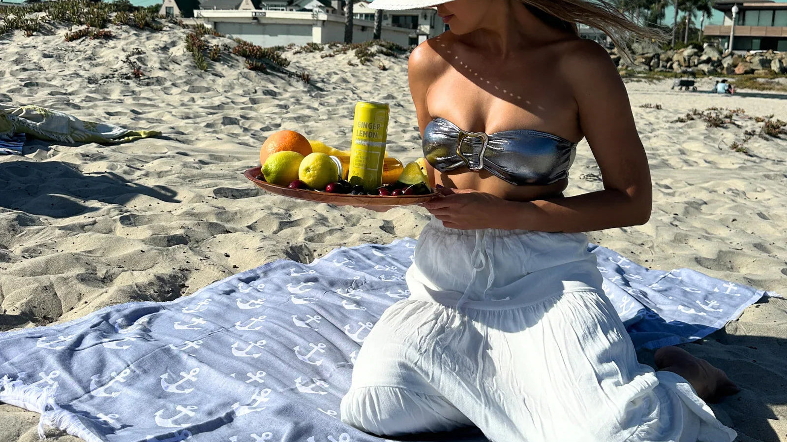 Woman on sandy beach with blue anchor-print Turkish cotton towel, holding fruit tray