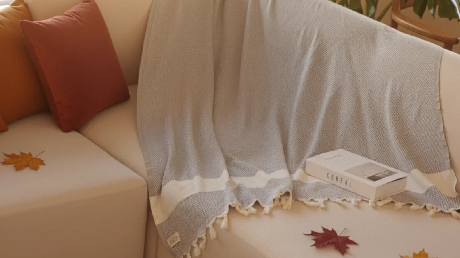 Cozy living room with a light blue Turkish throw blanket on a cream sofa, autumn leaves, and decorative pillows.