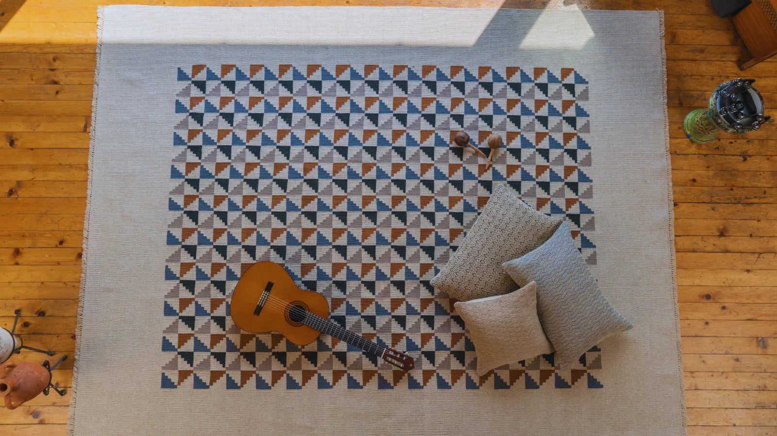 Hand-woven Turkish area rug with geometric pattern, pillows, and guitar on wooden floor