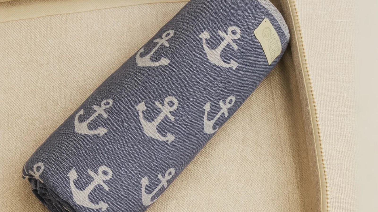 Folded blue beach towel with white anchor pattern in a beige storage basket