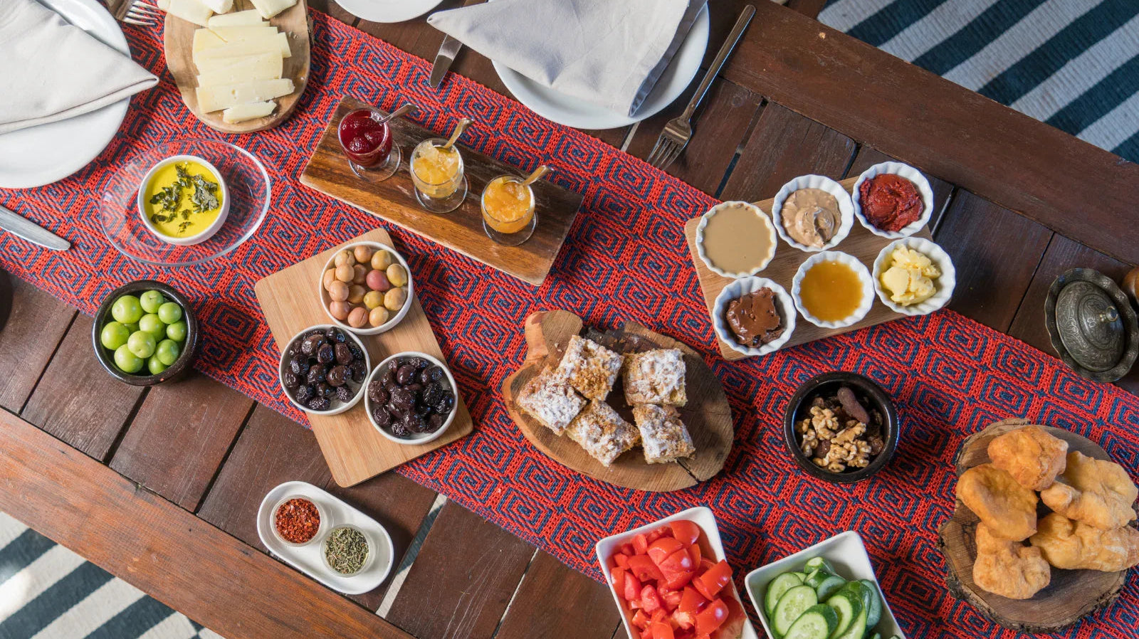 Traditional Turkish breakfast spread with cheeses, olives, jams, honey, vegetables, and pastries on a wooden table.
