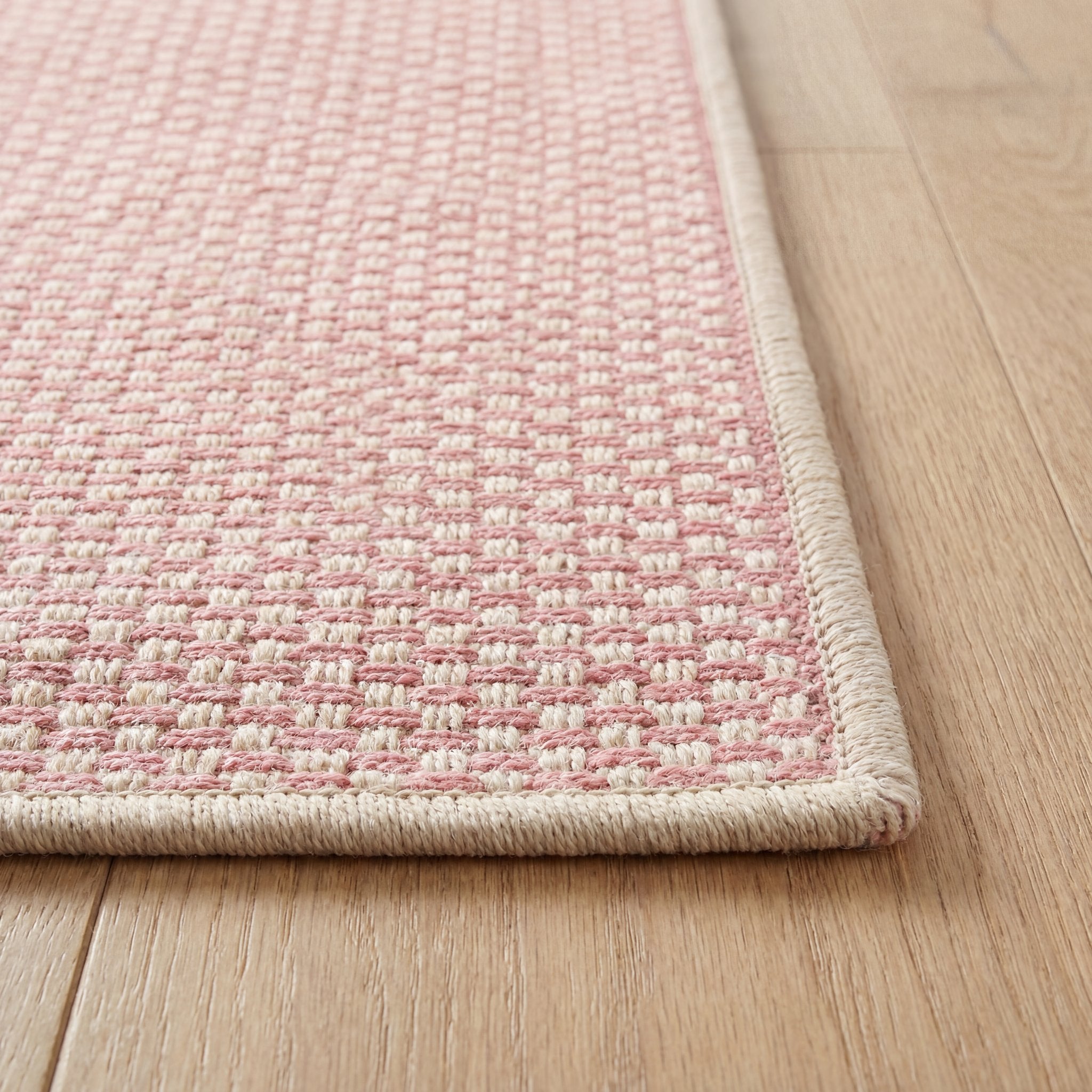 Close-up of the bound edge and low pile of the pink geometric check runner rug