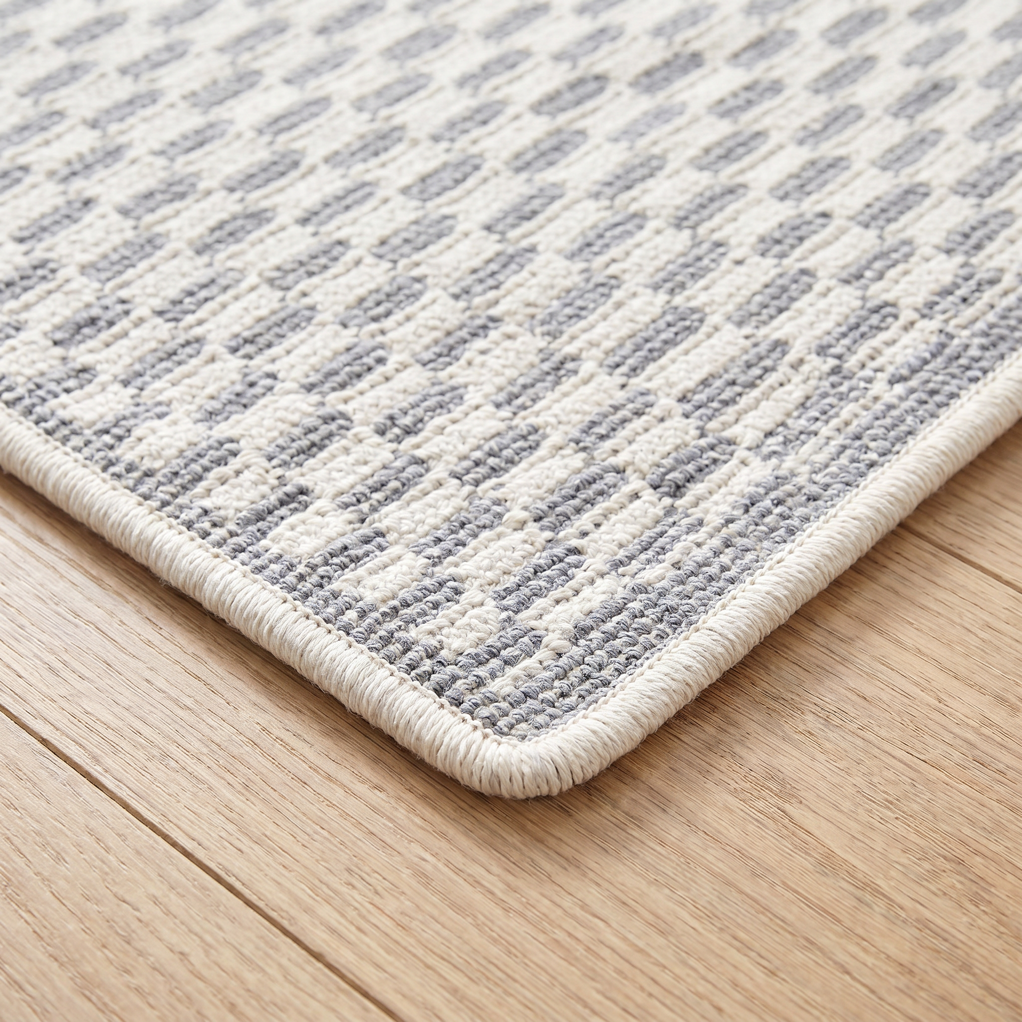 Close-up of the bound edge and low pile of the light gray geometric check runner rug