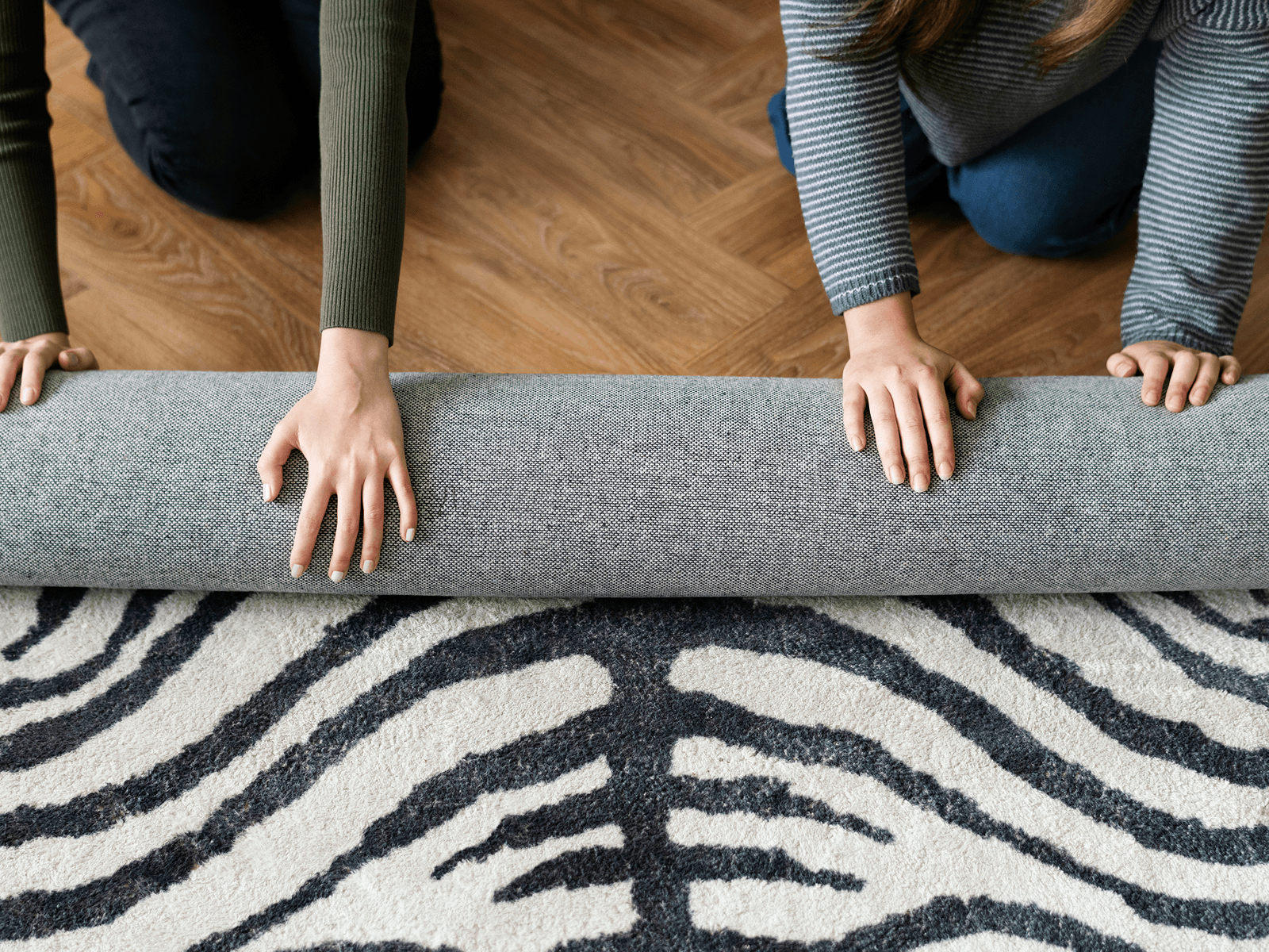 Hands rolling out a washable area rug with a black and white zebra pattern on hardwood floor