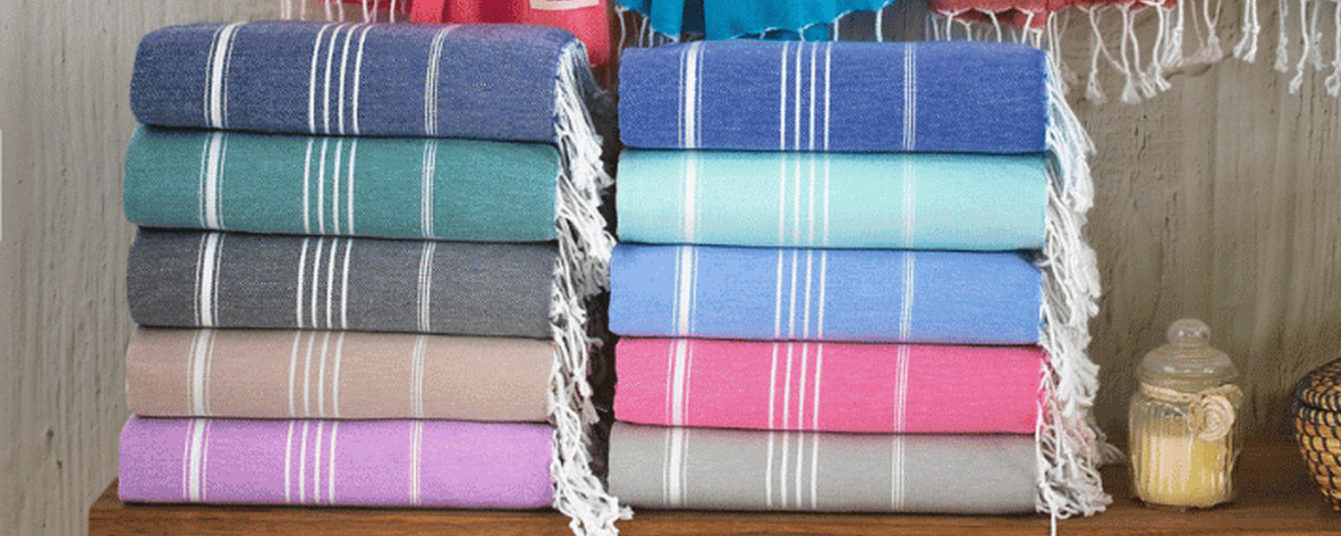 Stacked colorful Turkish cotton towels with fringe, displayed indoors on a wooden surface