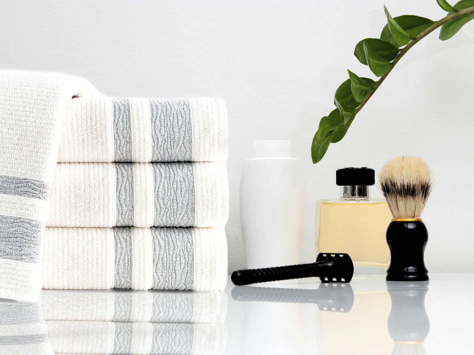 Stack of Turkish cotton towels with a razor, shaving brush, and toiletries on a bathroom counter.