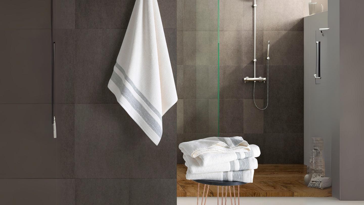 Stack of Turkish cotton towels and one hanging in modern bathroom with dark tiles