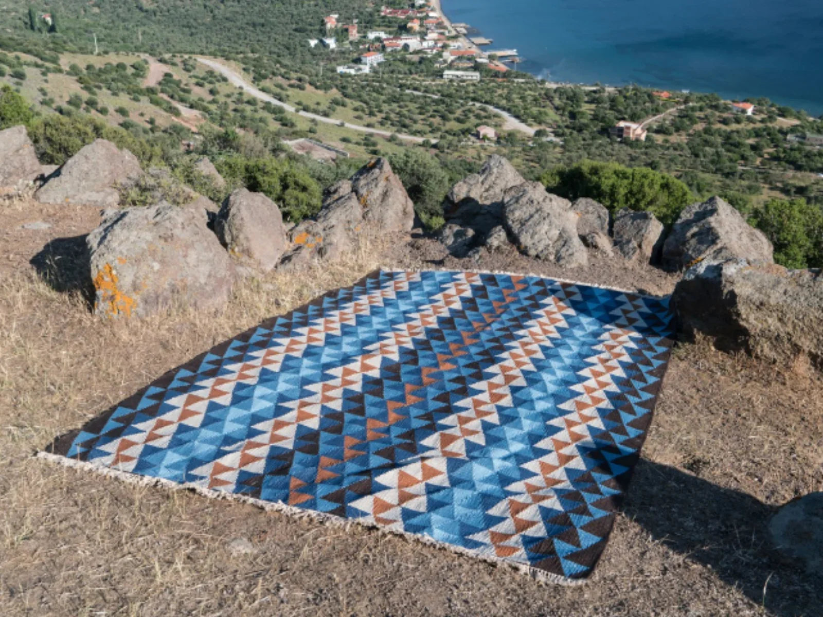 Geometric blue and brown Turkish washable area rug displayed outdoors with coastal view