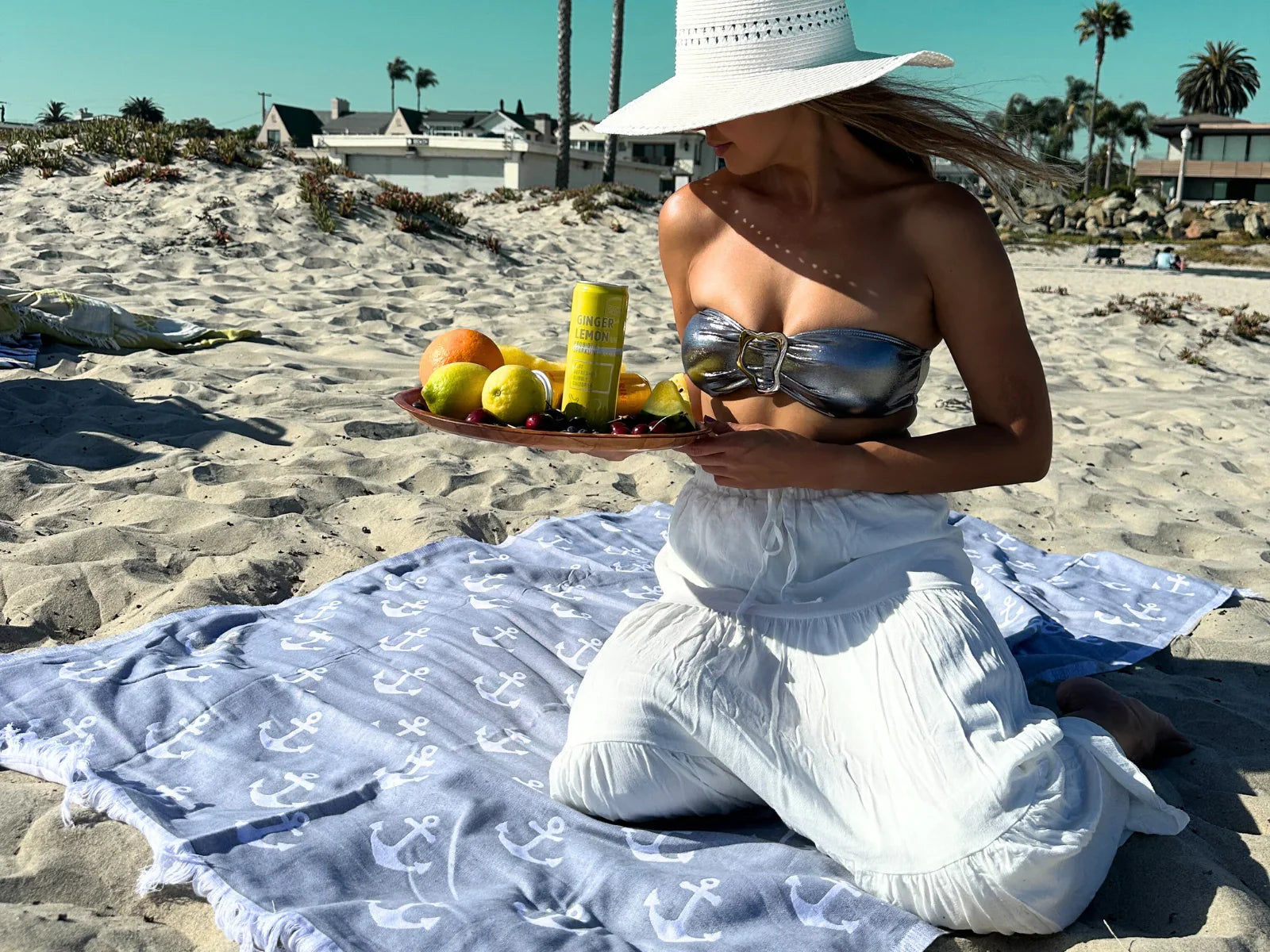 Woman on sandy beach with blue anchor-print Turkish cotton towel, holding fruit tray