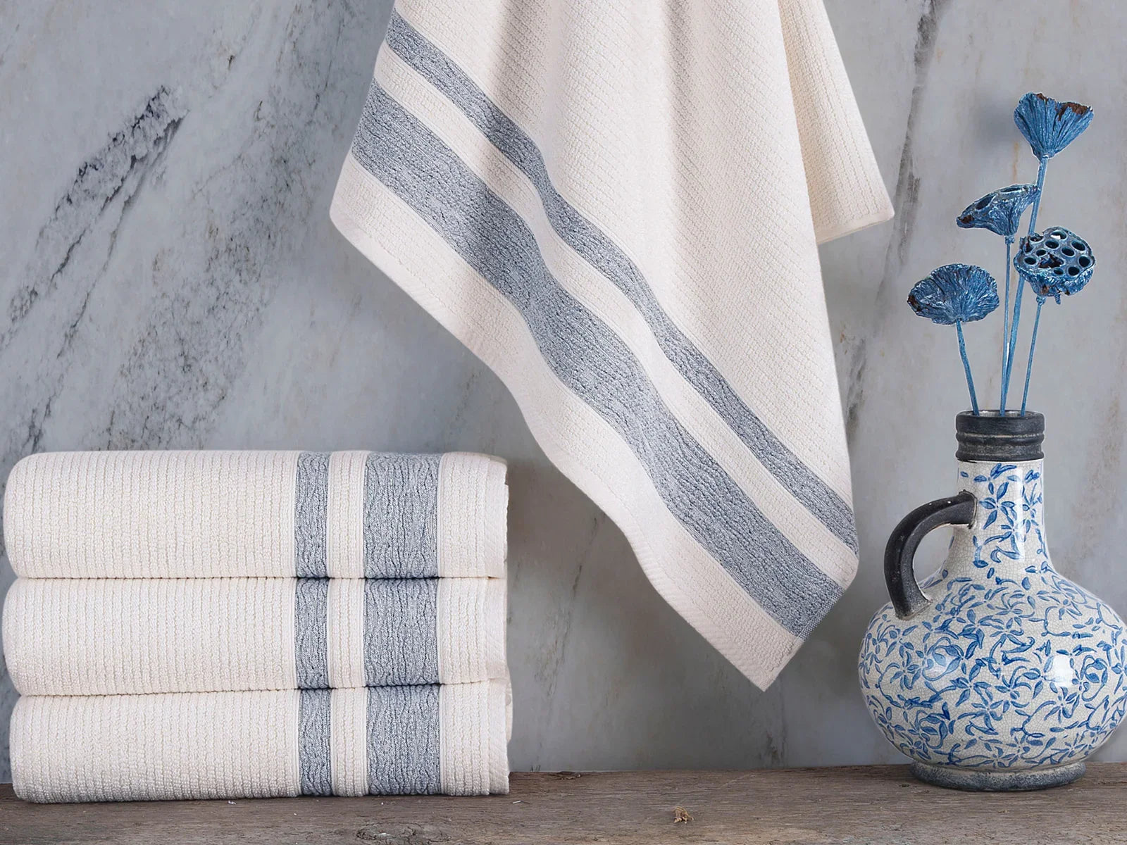 Stack of Turkish cotton towels with grey stripes, blue floral vase on marble background