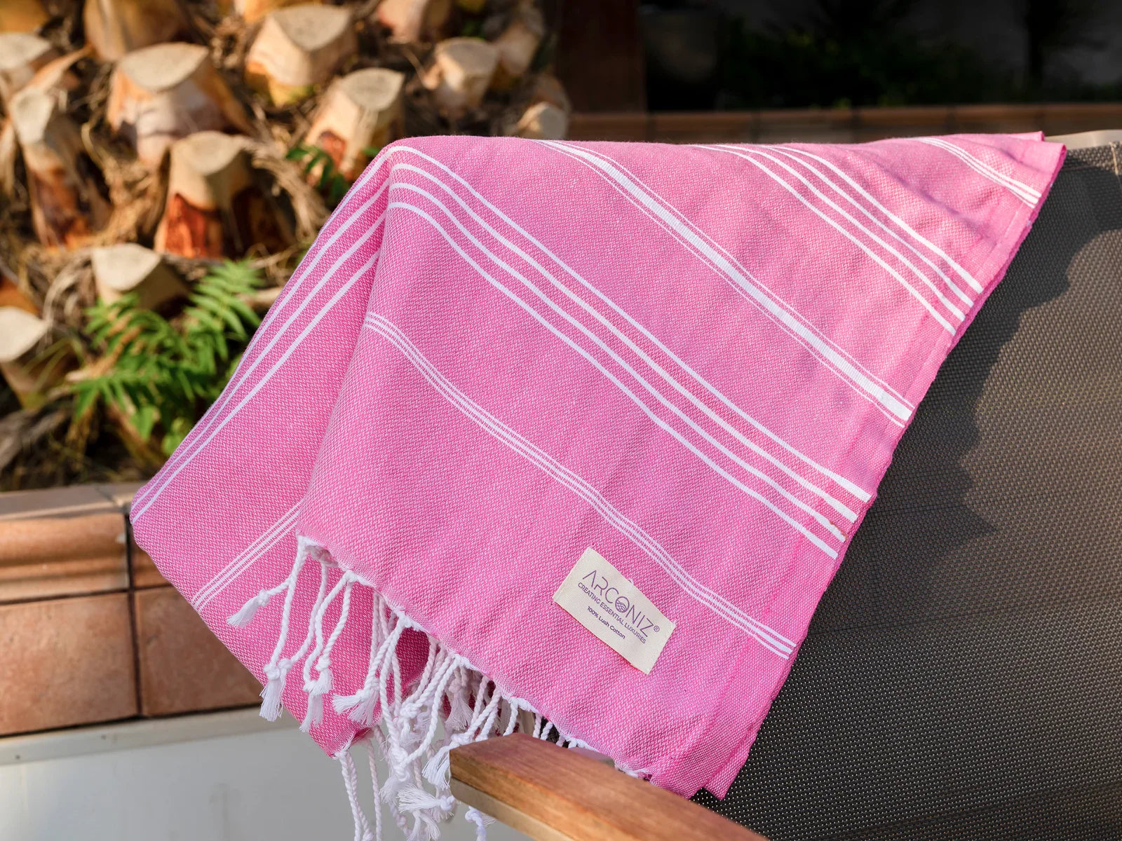 Pink Turkish cotton towel with white stripes and fringes draped over a chair outdoors