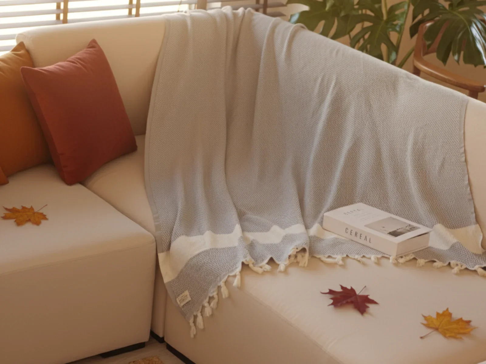 Cozy living room with a light blue Turkish throw blanket on a cream sofa, autumn leaves, and decorative pillows.