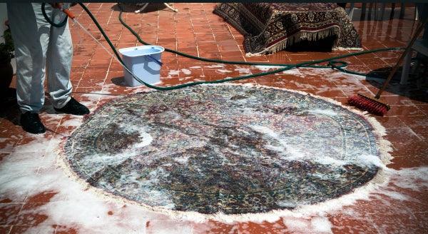 Deep cleaning a round Turkish washable area rug with soap, water, and brush outdoors