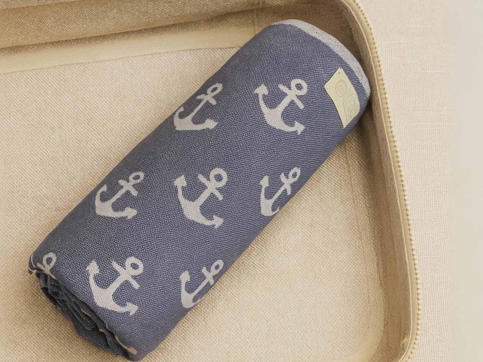 Folded blue beach towel with white anchor pattern in a beige storage basket
