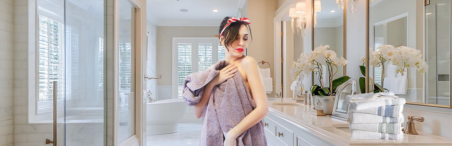Woman in luxury bathroom wrapped in a soft ribbed Turkish cotton towel next to stacked towels