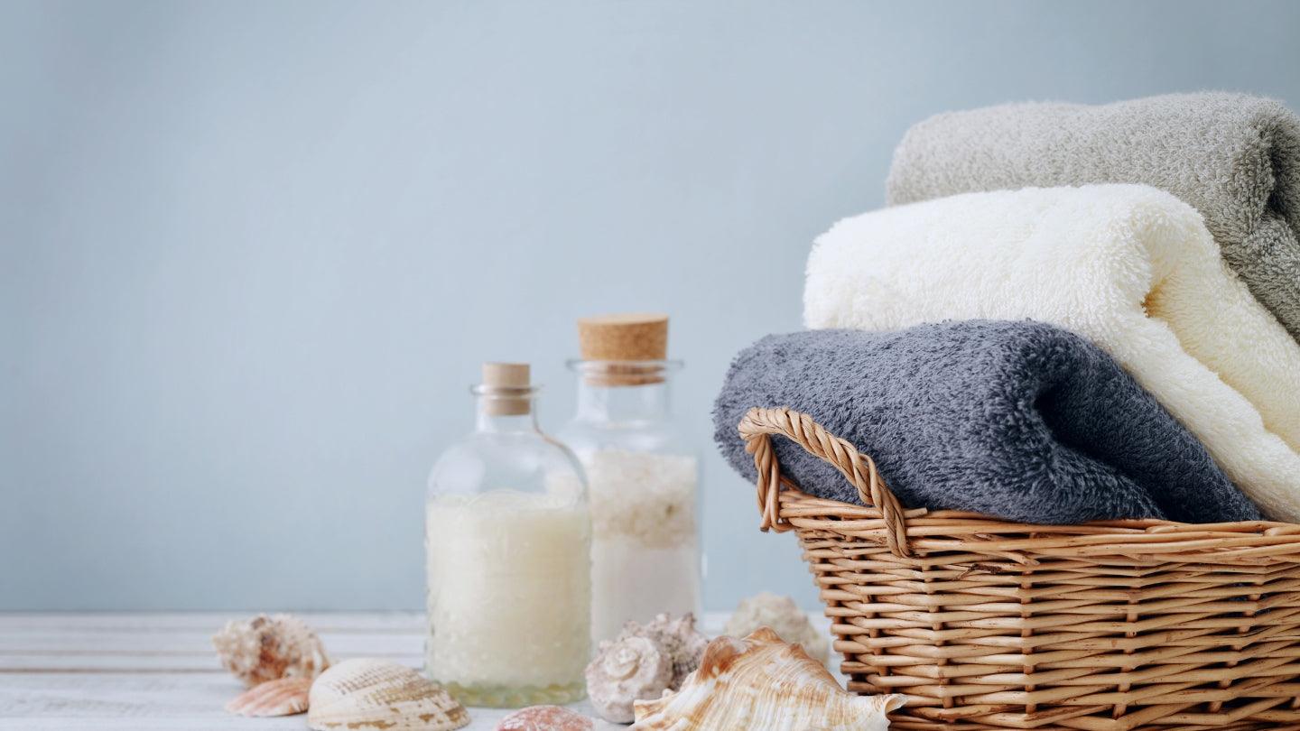 Turkish cotton towels in a wicker basket beside spa bottles and seashells on a wooden surface