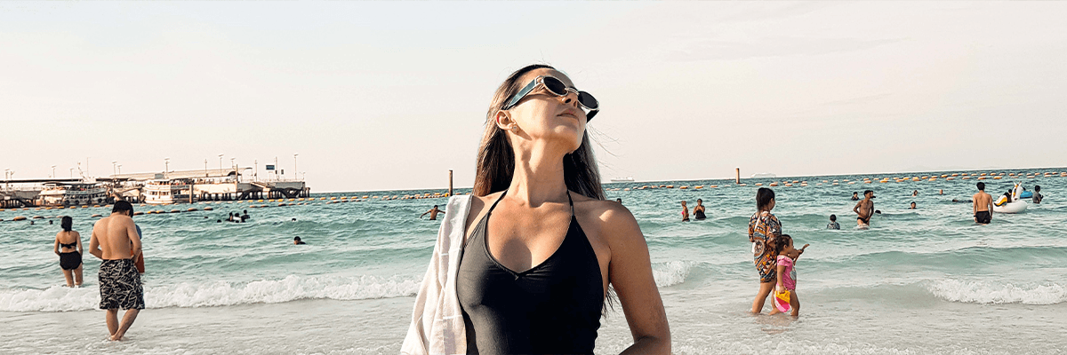Premium Beach Towels, woman enjoying the beach with a premium beach towel on her shoulder under a sunny sky.
