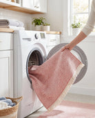Pink washable runner rug being loaded into a home washing machine